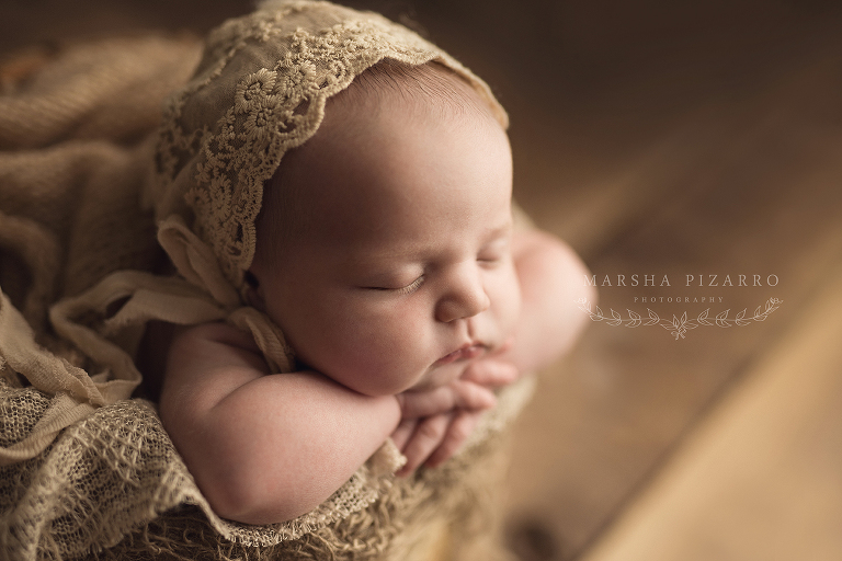 newborn resting on arms with lace hat